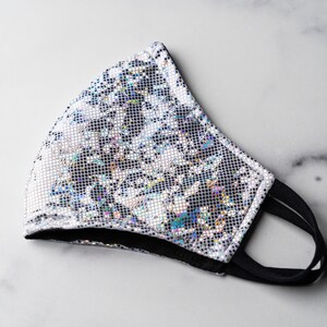 May include: A silver iridescent face mask with a black elastic band. The mask has a geometric pattern.