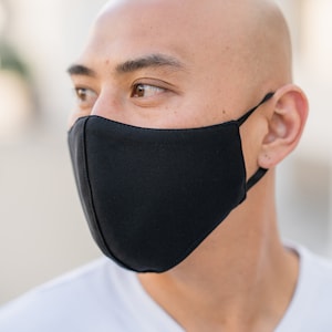 May include: A man wearing a black face mask. The mask covers his nose and mouth. He is looking to the right.
