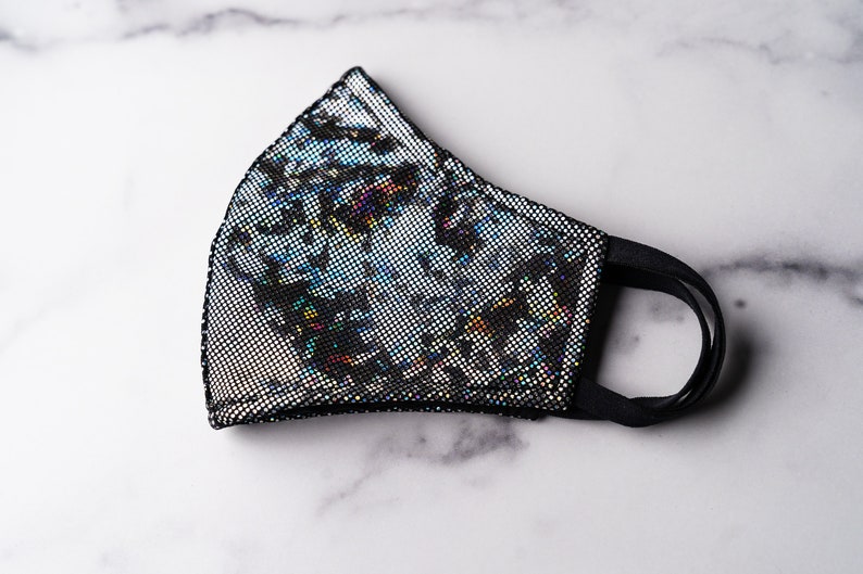 May include: A black face mask with a silver iridescent pattern. The mask has a black elastic band.