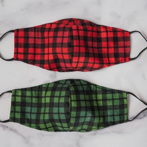 May include: Two face masks with adjustable ear loops. One mask is red and black plaid, the other is green and black plaid. Both masks are made of fabric and have black elastic ear loops.