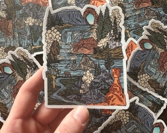 May include: A collection of stickers featuring a detailed landscape design. The stickers depict a scenic view with mountains, waterfalls, trees, and a bear. The color palette includes shades of blue, green, brown, and orange.