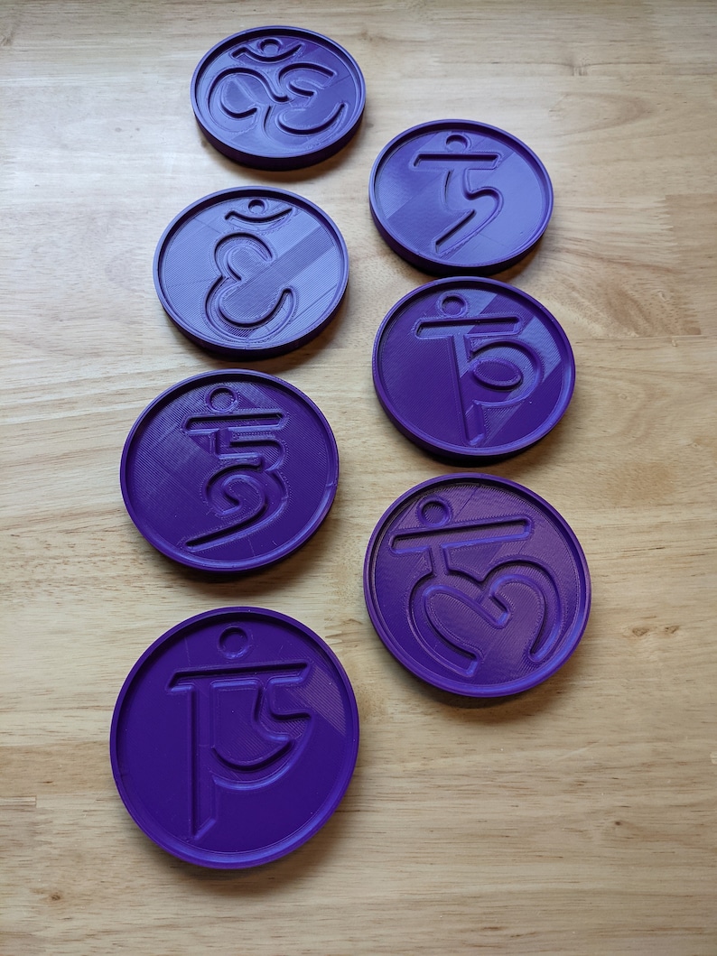 May include: Seven purple round coasters with different symbols, including the Om symbol, on a wooden surface.