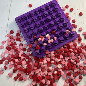 Könnte beinhalten: Lilafarbener Plastikform mit herzförmigen Vertiefungen, gefüllt mit rosa und roten Herzbonbons.