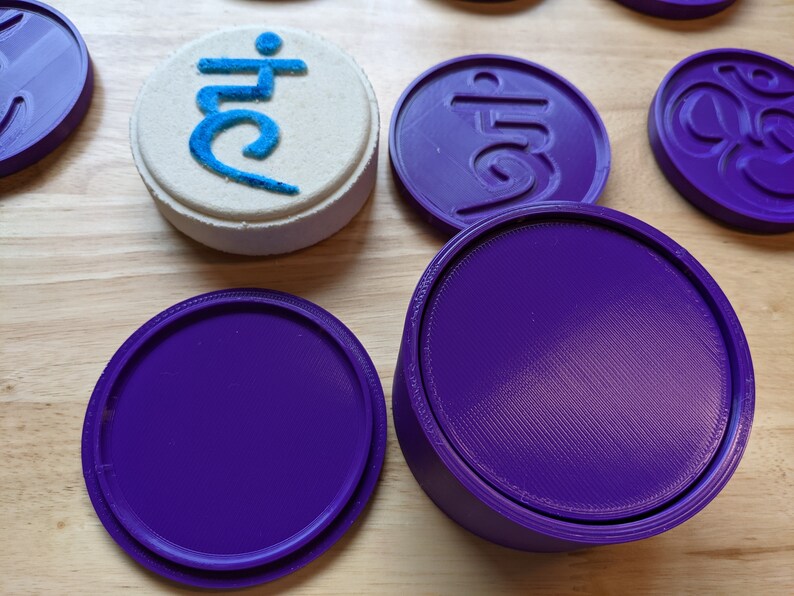 May include: A set of five purple round coasters with a raised design. One coaster has the Sanskrit symbol "Om" in the center. Another coaster has the Sanskrit symbol "Aum" in the center. The remaining three coasters are plain.