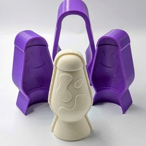 May include: A white lava lamp shaped mold with a purple silicone mold surrounding it. The silicone mold is in three pieces, two of which are shaped like the lava lamp and one that is a ring.