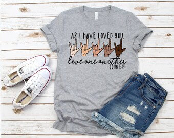 May include: Grey t-shirt with the text "As I have loved you, love one another John 13:34" and a row of hands in different skin tones signing the word "love" in American Sign Language.