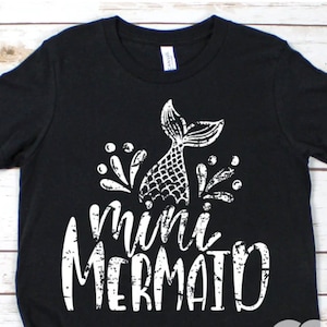 May include: Black t-shirt with a white graphic of a mermaid tail and the text "mini mermaid" in a distressed font.