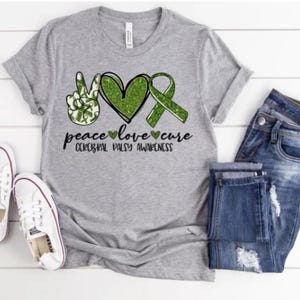 May include: Gray t-shirt with a green peace sign, heart, and ribbon. The text reads "peace love cure Cerebral Palsy Awareness".