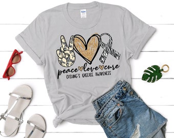 May include: A gray t-shirt with a peace sign, heart, and ribbon design. The text "peace love cure" is printed below the design. The text "Cushing's Disease Awareness" is printed below the text.