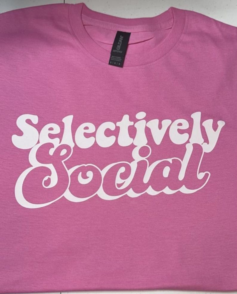 May include: Pink t-shirt with the text "Selectively Social" in white, retro-style lettering.