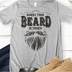May include: Gray t-shirt with the text "Sorry, this beard is taken" and a black and white illustration of a beard.