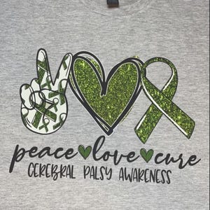 May include: A grey t-shirt with a green glitter peace sign, heart, and ribbon. The text "peace love cure" and "Cerebral Palsy Awareness" is printed on the shirt.