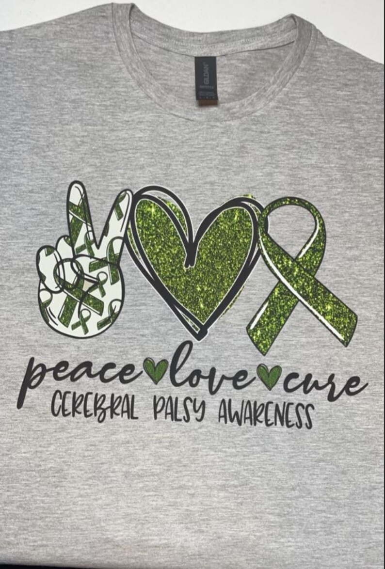 May include: A grey t-shirt with a green glitter peace sign, heart, and ribbon. The text "peace love cure" and "Cerebral Palsy Awareness" is printed on the shirt.