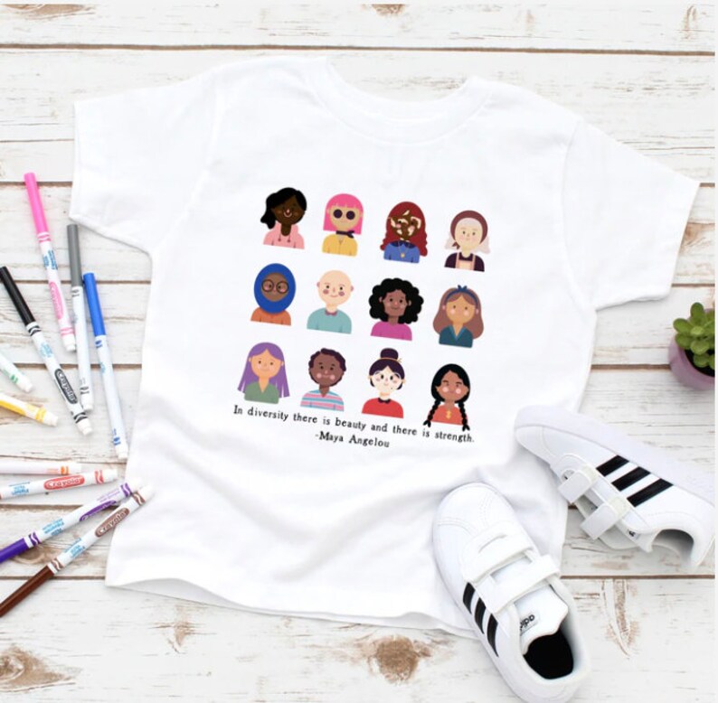 May include: White t-shirt with a graphic of diverse people and the quote "In diversity there is beauty and there is strength. -Maya Angelou".