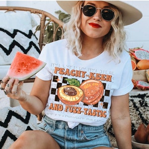 May include: White t-shirt with a peach graphic and the text "Peachy-Keen and Fuzz-Tastic".