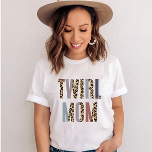 Könnte beinhalten: Weißes T-Shirt mit dem Text "TWIRL MOM" in Leopardenmuster und bunten Buchstaben.