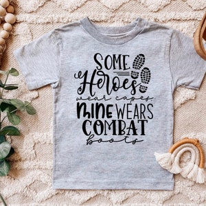 May include: Gray short-sleeved t-shirt with black text that reads "Some heroes wear capes, mine wears combat boots" and a graphic of two boot prints.