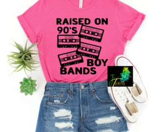 May include: Pink t-shirt with the text "RAISED ON 90'S BOY BANDS" in black. The text is surrounded by five black and white cassette tapes with the names of boy bands printed on them.