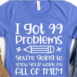 May include: A blue t-shirt with white text that reads "I got 99 Problems ÷ * You're going to show your work on ALL OF THEM".