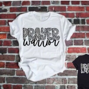 May include: White t-shirt with the words "Prayer Warrior" in black lettering. The word "Prayer" is made up of a leopard print pattern.