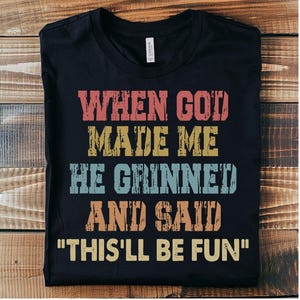 May include: Black t-shirt with a vintage-style graphic that reads "When God made me he grinned and said "This'll be fun".