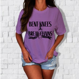 May include: Purple t-shirt with the text "Bent Knees Break Chains" in black lettering. The text is accompanied by a graphic of two hands clasped together with chains breaking apart.