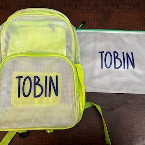 May include: A clear mesh backpack and matching pencil case, both featuring the name "TOBIN" in navy blue. The backpack has neon green detailing and straps. The pencil case has a green zip.