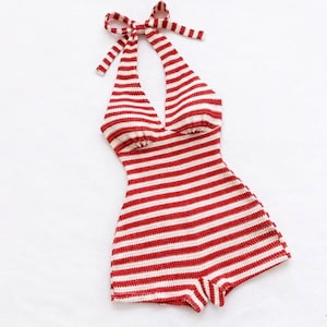 May include: A red and white striped halter-style romper. The romper features a halter neck with a bow and a shorts-style bottom. The garment is made of a knitted material and is displayed on a white background.