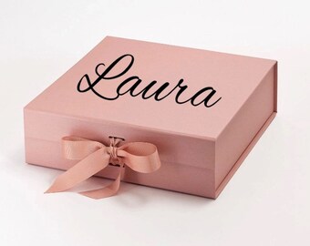 May include: A blush pink gift box with a satin ribbon tied in a bow. The box has the name "Laura" printed in black cursive on the top.