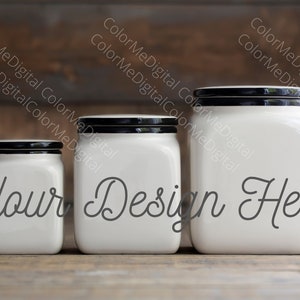 May include: Three white ceramic jars with black lids of varying sizes are displayed on a wooden surface. The jars have a square shape and the text "Your Design Here" is written on the front in a cursive font. The background is a blurred wooden wall.