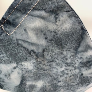 May include: Close-up of a gray and white fabric with a subtle pattern. The fabric has a rough texture and a white seam running along the top edge.