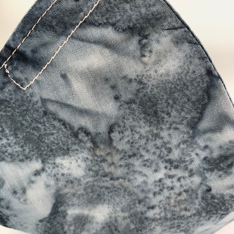 May include: Close-up of a gray and white fabric with a subtle pattern. The fabric has a rough texture and a white seam running along the top edge.