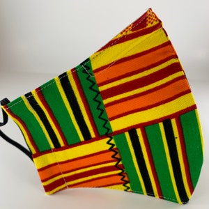 May include: A face mask with a colorful geometric pattern in shades of green, yellow, red, and black. The mask is made of fabric and has a three-dimensional shape.