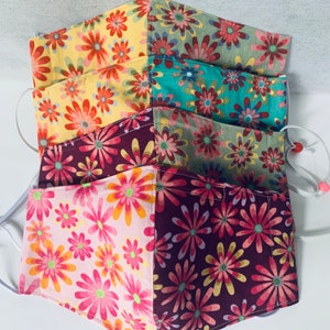 May include: Set of four fabric face masks with a floral pattern. The masks are made of a patchwork of different floral prints in shades of pink, yellow, green, and purple.