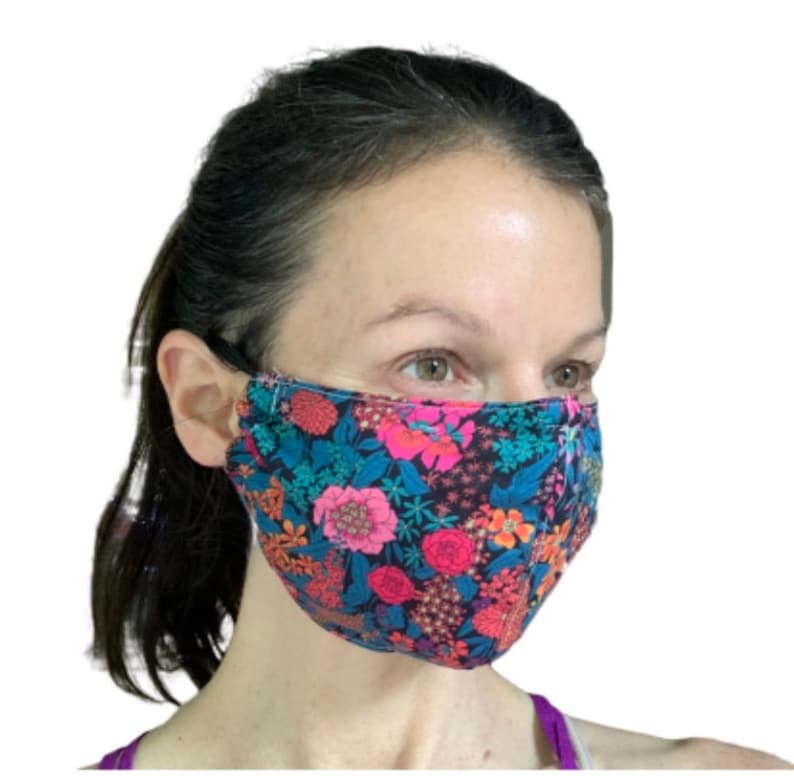 May include: A person wearing a black face mask with a floral pattern featuring pink, red, and blue flowers on a dark blue background.
