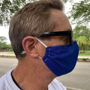 May include: A person wearing a royal blue face mask with white elastic ear loops and black sunglasses.