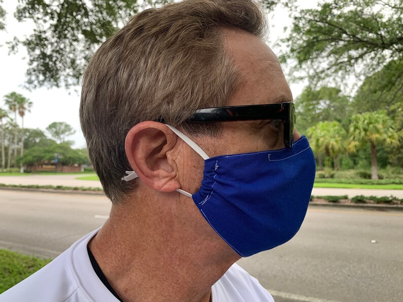 May include: A person wearing a royal blue face mask with white elastic ear loops and black sunglasses.