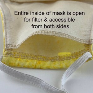 May include: A yellow fabric face mask with a white elastic band. The inside of the mask is open for a filter and is accessible from both sides. The text "Entire inside of mask is open for filter & accessible from both sides" is printed on the mask.