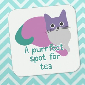 May include: A white coaster featuring a purple and teal cat illustration. The text "A purrfect spot for tea" is written below the cat.