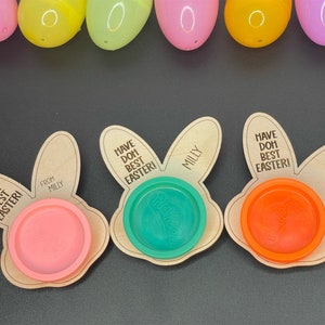 May include: Three wooden bunny-shaped Easter treat holders with the text "Have Doh Best Easter!" and "From Milly". Each holder has a small plastic container for play dough, one is pink, one is green, and one is orange.