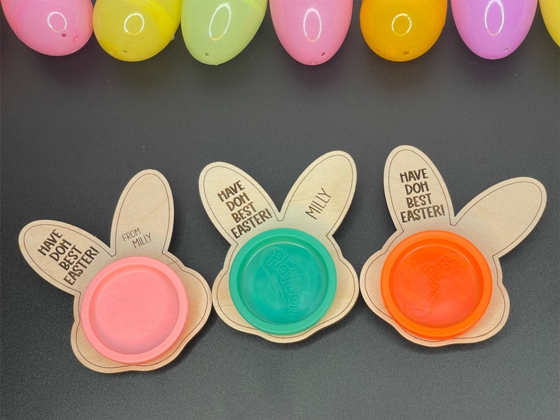 May include: Three wooden bunny-shaped Easter treat holders with the text "Have Doh Best Easter!" and "From Milly". Each holder has a small plastic container for play dough, one is pink, one is green, and one is orange.