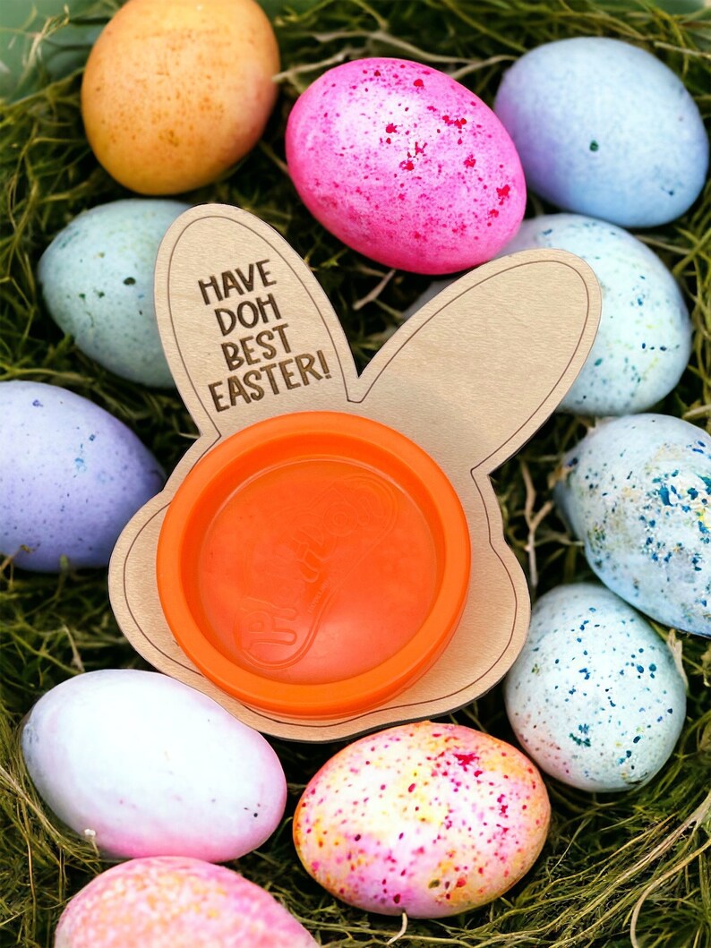May include: A wooden bunny-shaped Easter egg holder with the text "Have Doh Best Easter!" and an orange plastic container inside. The holder is surrounded by colorful Easter eggs.