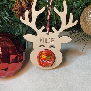 Peut inclure: Ornement de renne en bois avec le nom Khloe &eacute;crit dessus. Le renne a un bonbon rouge et blanc dans la bouche qui dit Lindor.