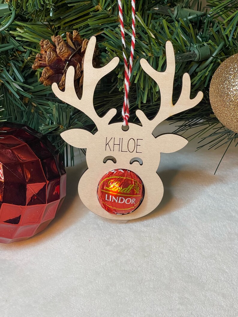 Peut inclure: Ornement de renne en bois avec le nom Khloe &eacute;crit dessus. Le renne a un bonbon rouge et blanc dans la bouche qui dit Lindor.
