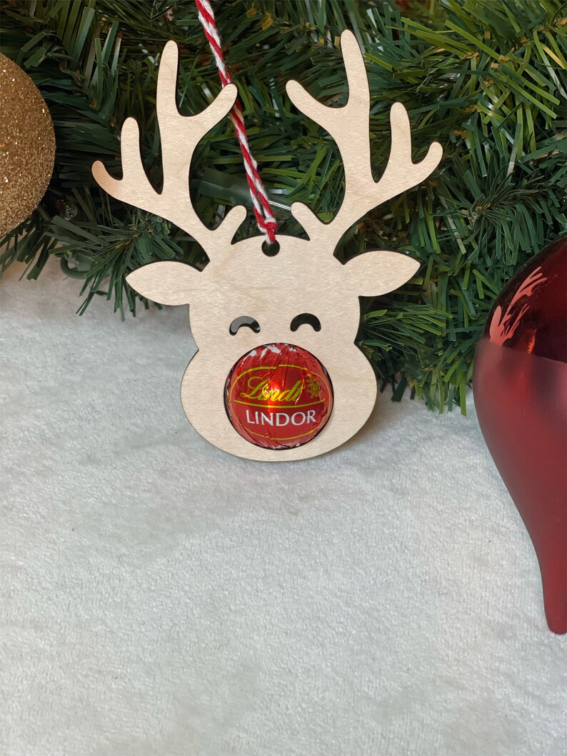 Peut inclure: Ornement de renne en bois avec une truffe au chocolat Lindor rouge pour le nez. L'ornement est suspendu &agrave; une ficelle rouge et blanche.