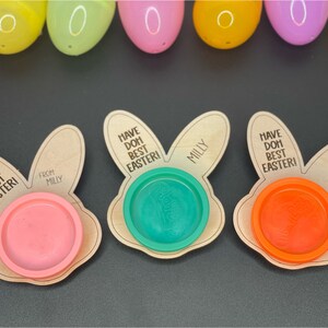 May include: Three wooden bunny-shaped Easter treat holders with the text "Have Doh Best Easter!" and "Milly" on them. Each holder has a small plastic container for playdough.