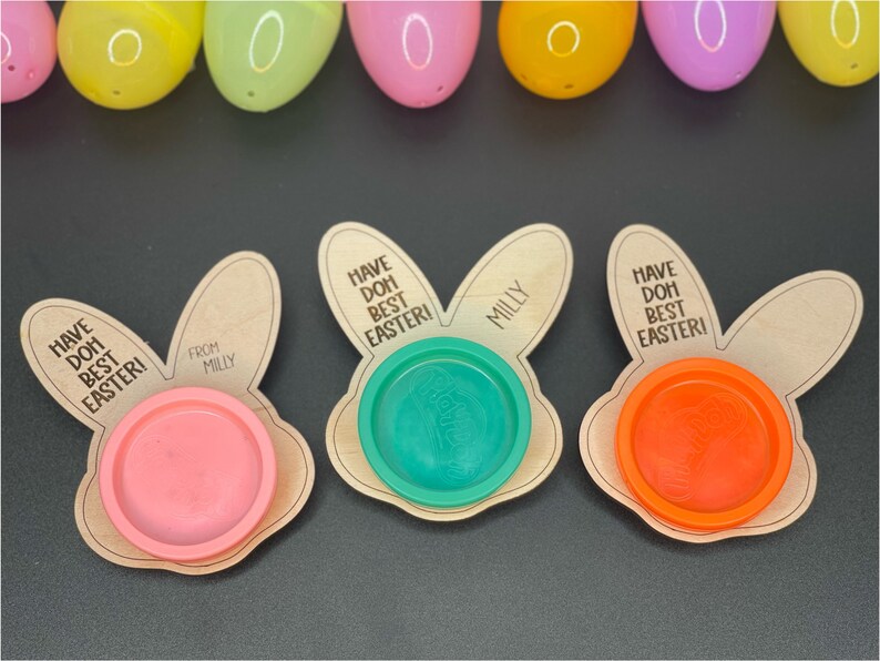 May include: Three wooden bunny-shaped Easter treat holders with the text "Have Doh Best Easter!" and "Milly" on them. Each holder has a small plastic container for playdough.