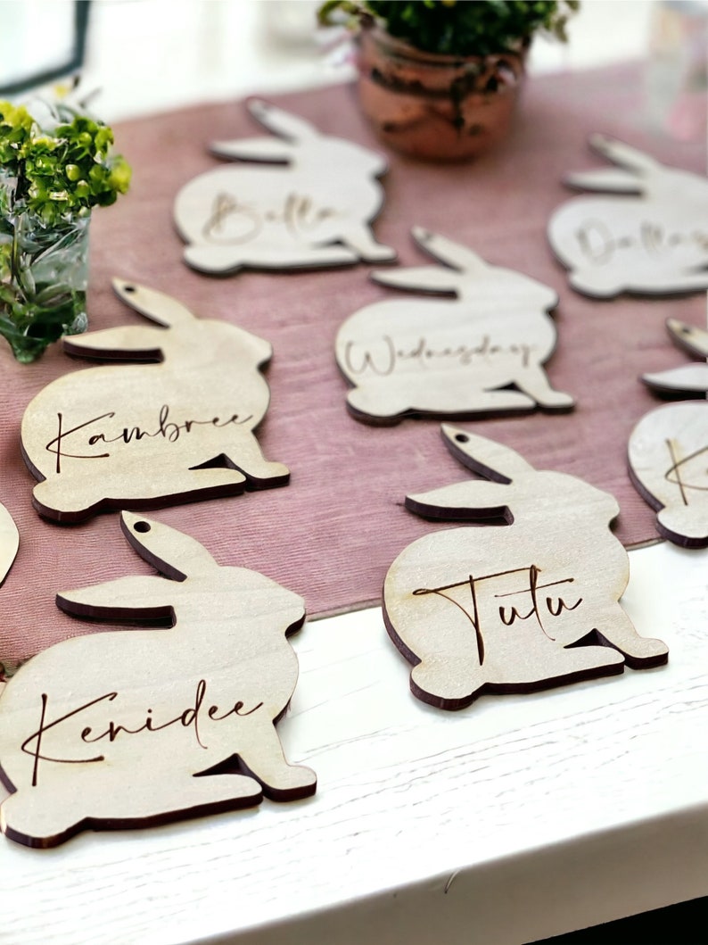 May include: Wooden bunny rabbit place card holders with names written on them. The names are: Kambree, Kenidee, Tutu, Wednesday, Belle, and Dolly.