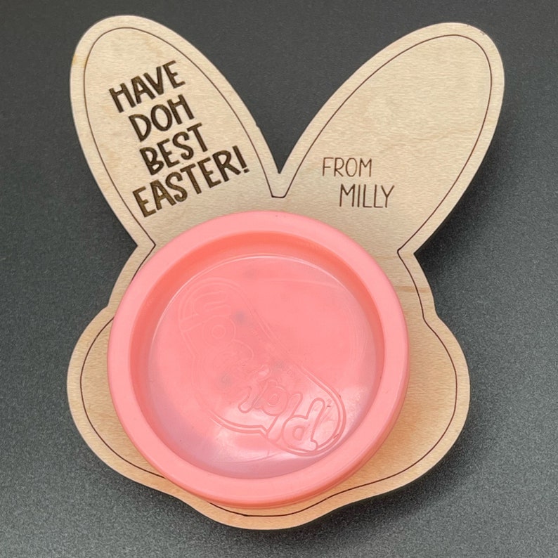 May include: A wooden bunny-shaped Easter craft with the text "Have Doh Best Easter!" and "From Milly". A pink play dough container is in the center.