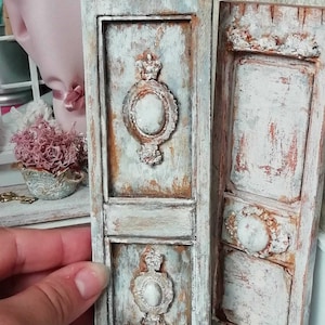 Può includere: Due porte in legno bianco invecchiato con dettagli decorativi, tra cui una corona e un design ovale. Le porte sono dipinte in uno schema di colori blu chiaro e bianco.